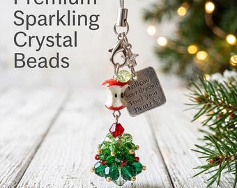 Könnte beinhalten: Ein dekorativer Hängeanhänger mit einem Weihnachtsbaum aus grünen Kristallperlen, einem rot-weißen Apfelgriebsch-Anhänger und einem quadratischen silbernen Metallschild mit der Gravur "follow your dreams Trust your heart" und einem Herz.