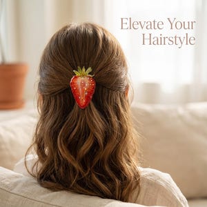 May include: A strawberry-shaped hair clip with a red body, green leaves, and small gold star accents. The hair clip is positioned in the center of brown hair. The text "Elevate Your Hairstyle" is visible in the upper right corner of the image.