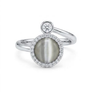 May include: A silver-toned bypass ring featuring a large, round, grey cat's eye stone set in a halo of small clear stones. A single, smaller round clear stone is set in a bezel above the main circular setting on the polished metal band.