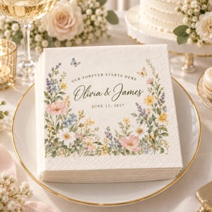 May include: A stack of square white paper napkins featuring a colorful watercolor floral border with butterflies. The text reads "OUR FOREVER STARTS HERE", "Olivia & James", and "JUNE 12, 2027" in a black serif and script font centered on the napkin.