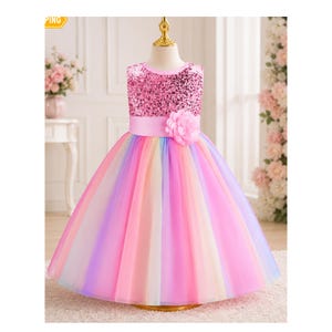 May include: A sleeveless dress featuring a bodice covered in shimmering pink sequins and a wide satin waistband adorned with a large fabric flower. The full-length skirt consists of multiple layers of multicolored tulle in pastel shades of pink, purple, and blue.