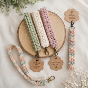 Puede incluir: Cuatro llaveros de muñeca tejidos a ganchillo en verde salvia, crema, rosa empolvado y un hilo multicolor en tonos melocotón y azul. Cada uno incluye un mosquetón de metal y una etiqueta de cartón festoneada con el texto 'Handmade with heart, just for you.'