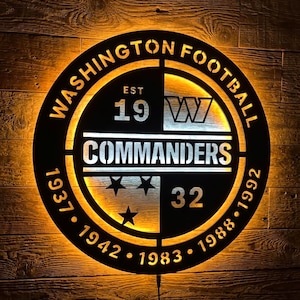 May include: A circular black metal wall sign featuring the Washington Commanders logo with warm amber backlighting. The text reads WASHINGTON FOOTBALL COMMANDERS, EST 19, 1937, 1942, 1983, 1988, 1992, and 32, with a W logo and three stars.