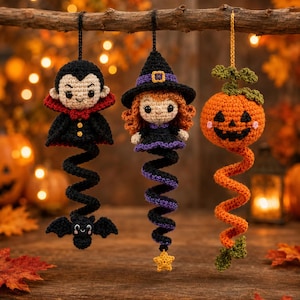 Puede incluir: Tres adornos de Halloween tejidos a ganchillo colgados de una rama. A la izquierda, un vampiro con capa negra y un murciélago. En el centro, una bruja con sombrero negro y una estrella amarilla. A la derecha, una calabaza naranja con hojas verdes.