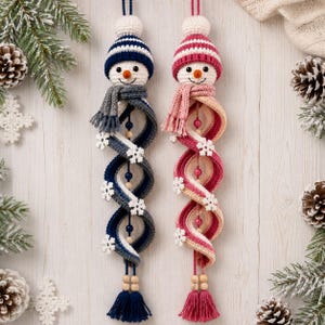 May include: Two hanging crochet snowman ornaments with spiral bodies. One features a blue and white striped hat and scarf with blue beads, the other a pink and white striped hat and scarf with pink beads. Both have white snowflake accents.