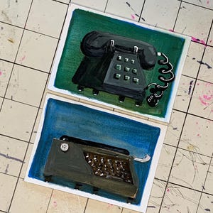 May include: Two square paintings. The top painting features a black rotary phone on a green background. The bottom painting shows a black typewriter on a blue background. Both paintings have white borders.