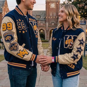 May include: Two navy blue and beige varsity jackets featuring embroidered patches. The left jacket displays the number 99, a wildcat mascot, and the text Wildcats. The right jacket features the name Maya, a wildcat mascot, and star-shaped patches.