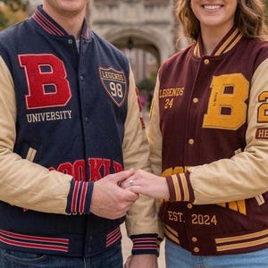 May include: Two varsity jackets featuring long tan sleeves and ribbed cuffs. The left jacket is navy blue with a red letter B, the text UNIVERSITY, and a shield patch with LEGENDS 98. The right jacket is maroon with a yellow letter B, the text LEGENDS 24, and EST. 2024.