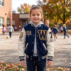 May include: A navy blue and cream varsity jacket featuring a large yellow letter W on the chest, a wildcat mascot patch on the right sleeve, and the text MIA WILDCATS EST. 2017. The jacket has a snap-button front, striped ribbed cuffs, and a gray hood.