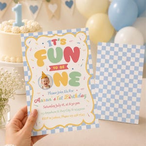 May include: A rectangular birthday invitation card featuring a light blue and white checkered border. The text reads IT'S FUN TO BE ONE, Please Join Us For Aaron's 1st Birthday, Saturday July 18, at 6:30 pm, 123 Anywhere St. Any City, St 12345xxx, RSVP to Joshua, Phone 123-456-7345.