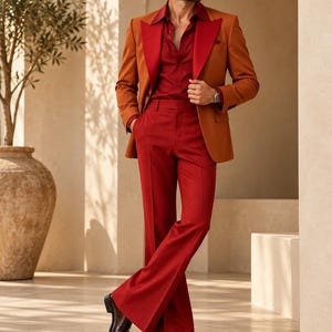 Può includere: Un blazer color ruggine con ampi revers indossato sopra una camicia rossa scura abbottonata e pantaloni rossi a zampa coordinati. L'insieme è completato da scarpe eleganti in pelle marrone scuro e occhiali da sole scuri.