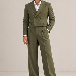 Op de afbeelding: Een olijfgroene, dubbelrijige, korte blazer met brede revers en een bijpassende broek met hoge taille en wijde pijpen. De outfit wordt gecombineerd met een wit overhemd met kraag en lichtgekleurde leren loafers voor een gecoördineerde look.
