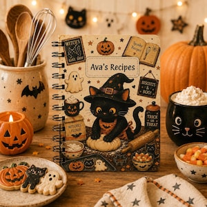 Puede incluir: Un cuaderno de recetas de espiral titulado Ava's Recipes que muestra a un gato negro con sombrero de bruja y delantal amasando. La portada incluye ilustraciones de calabazas, fantasmas, un saco de harina y letreros de Witch's Bake Shop y Biscuits & Boo.