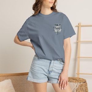 Può includere: Una t-shirt a maniche corte color blu ardesia con una piccola grafica sul lato sinistro del petto. La grafica è un disegno in bianco e nero con l'icona di un fulmine e il testo "CHAOS THEORY" scritto in un carattere stilizzato e usurato.