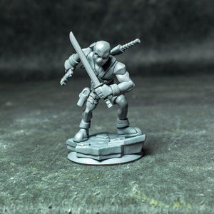May include: A gray unpainted miniature figurine of a masked character in a crouching stance, holding a sword in one hand and a pistol in the other, with a second sword sheathed on the back, standing on a textured rocky base.