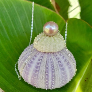 May include: A silver chain necklace with a purple and white sea urchin pendant and a pink pearl on top.