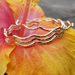 May include: Three gold-toned wavy bangles stacked on top of each other, resting on a pink and orange flower petal.