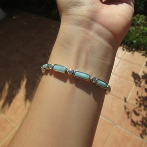 Könnte beinhalten: Ein silberfarbenes Armband mit abwechselnd rechteckigen hellblauen Steinen und kleinen runden, klaren Steinen. Das Armband besteht aus einer Reihe von Gliedern, die jeweils einen glatten, hellblauen rechteckigen Einsatz oder einen klaren Stein enthalten.