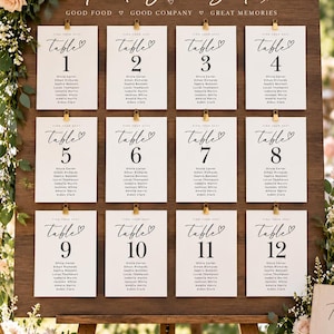 May include: A wooden seating chart display featuring twelve white rectangular cards clipped to a dark wood board. Each card displays the text "FIND YOUR SEAT", "table" with a heart icon, a large number from 1 to 12, and a list of names.