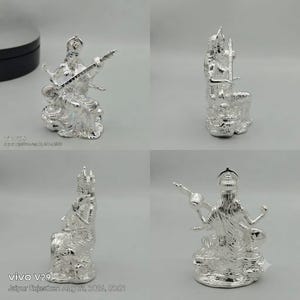 May include: A shiny silver-toned figurine depicting a seated deity playing a stringed instrument. The figure features intricate detailing on the clothing and jewelry, with four arms, a crown, and a base. The sculpture is shown from four angles.