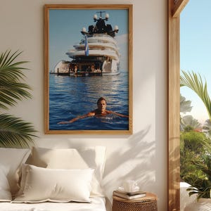 May include: A framed wall art print featuring a large white multi-deck yacht anchored in deep blue ocean water, with a person swimming in the foreground. The yacht has multiple levels, a dark upper structure, and a blue flag flying from the stern.