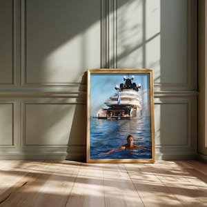 May include: A rectangular framed print featuring a large white yacht floating on deep blue water with a person swimming in the foreground. The yacht has multiple decks and a blue flag visible on the stern. The frame is a light wood color.