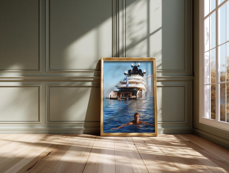 May include: A rectangular framed print featuring a large white yacht floating on deep blue water with a person swimming in the foreground. The yacht has multiple decks and a blue flag visible on the stern. The frame is a light wood color.