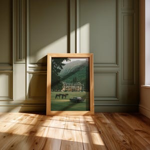 May include: A rectangular wooden picture frame containing a print of a large estate building situated on a grassy lawn with two horses and a vintage car. The frame is light brown with a natural wood grain finish and a simple, clean-lined border.