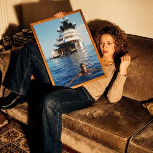 May include: A rectangular wooden-framed print featuring a large white yacht anchored in deep blue water with a person swimming in the foreground. The artwork captures a bright, sunny day at sea, showcasing the vessel's multi-level deck structure.
