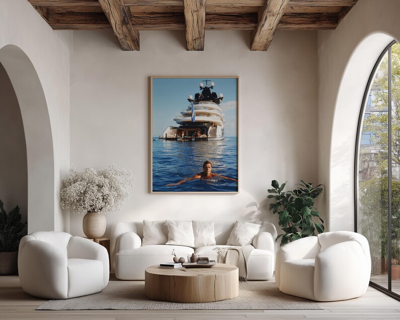 May include: A framed wall art print featuring a large white luxury yacht anchored in deep blue ocean waters with a person swimming in the foreground. The image captures the vessel's multi-level deck structure and the clear, calm sea surface.