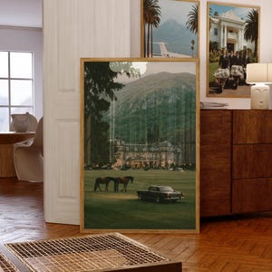 May include: A large framed wall art print featuring a landscape scene of a grand estate with a green lawn, two horses, and a vintage car. The image displays a mountain backdrop, tall trees, and warm lighting emanating from the building windows.