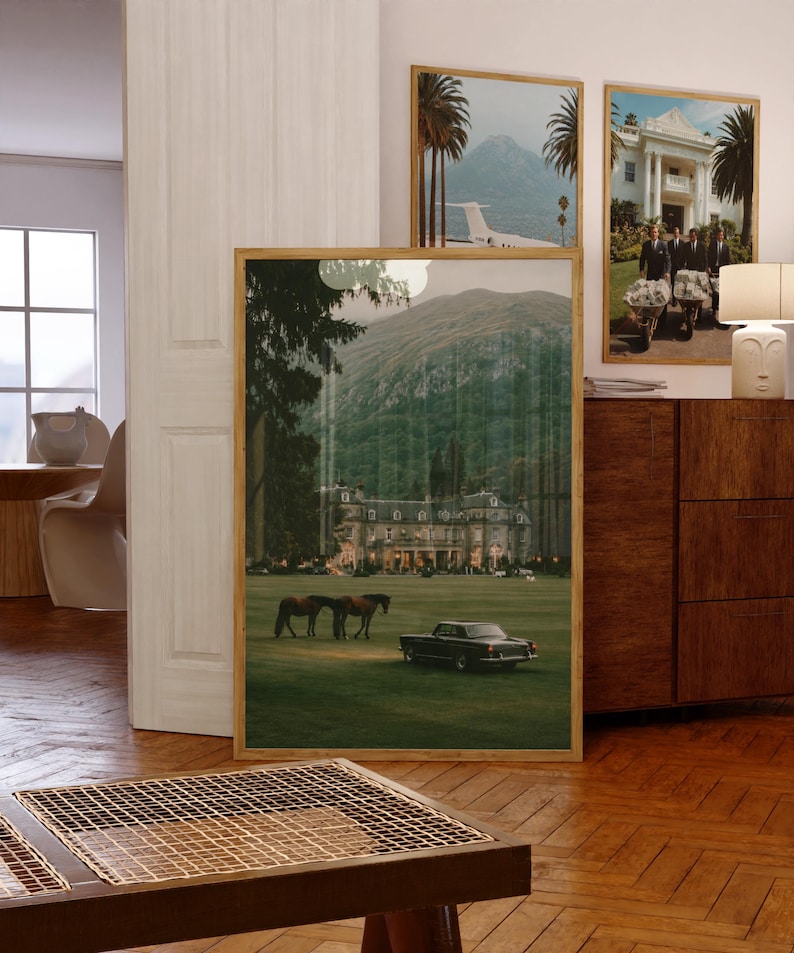 May include: A large framed wall art print featuring a landscape scene of a grand estate with a green lawn, two horses, and a vintage car. The image displays a mountain backdrop, tall trees, and warm lighting emanating from the building windows.