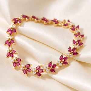 May include: A gold bracelet featuring a repeating leaf-like pattern composed of marquise-cut deep pink rubies and small round clear white diamonds. The jewellery piece is arranged in a circular shape, showcasing a delicate and symmetrical design.