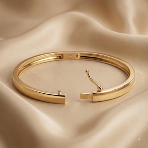 Peut inclure: Un bracelet jonc en or poli à la surface lisse et arrondie. Le bracelet présente un mécanisme d'ouverture à charnière avec un fermoir sécurisé et une petite goupille. L'intérieur de l'anneau en métal porte l'inscription 18K.