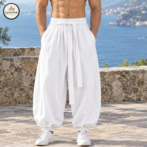 Puede incluir: Pantalones blancos de corte holgado con cintura elástica y cinturón de tela a juego, bolsillos laterales profundos y puños elásticos fruncidos en los tobillos. Los pantalones presentan una silueta amplia y relajada con acabado texturizado.