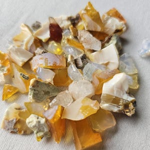 May include: A pile of small, rough, and irregular pieces of opal in various shades of yellow, orange, and white.