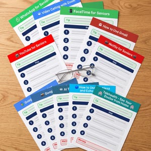 Op de afbeelding: Een verzameling instructiebladen voor senioren over onderwerpen zoals WhatsApp, FaceTime, Gmail, Netflix en Telehealth. Elk blad bevat genummerde stappen, tips en waarschuwingsvakken. Een zilveren leesbril ligt bovenop de stapel instructiebladen.