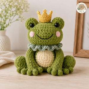 Peut inclure: Une peluche grenouille crochetée verte avec une couronne jaune sur la tête, un col à volants vert clair et un ventre crème. La grenouille a des yeux en plastique noir, des joues brodées roses et un large sourire noir incurvé sur le visage.