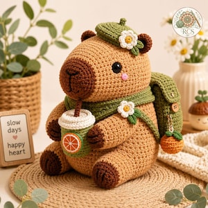 May include: A crocheted tan capybara plush toy wearing a green beret with a white flower, a green scarf, and a green backpack. The capybara holds a green cup with an orange slice graphic and has a small orange charm hanging from the backpack.
