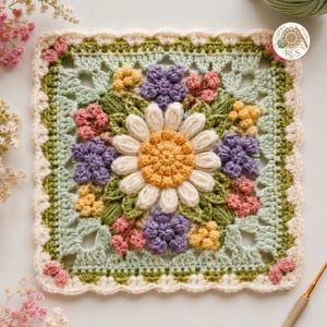 Può includere: Un motivo quadrato all'uncinetto con una grande margherita bianca centrale dal centro giallo, circondata da fiori più piccoli viola, rosa e gialli e foglie verdi. Il quadrato è bordato da un bordo smerlato color crema e include un logo.