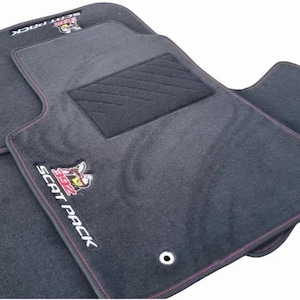 May include: A set of black automotive floor mats with red stitched edges. The mats feature a rectangular heel pad and an embroidered logo with a bee graphic and the text SCAT PACK 392. Two metal grommets are visible on the main floor mat.