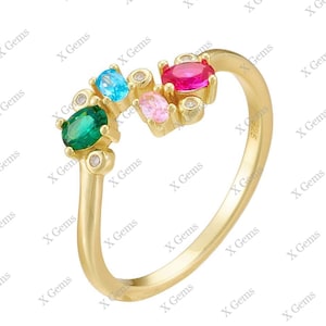 Può includere: Un anello in oro dal design aperto con un gruppo di pietre preziose a taglio ovale nei colori verde, azzurro, rosa e rosso, arricchito da piccole pietre rotonde trasparenti. La fascia è liscia e lucida, con la scritta S925 visibile all'interno.