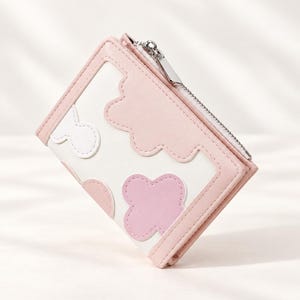 May include: A bi-fold wallet in white with light pink and pastel pink cloud-shaped and flower-shaped appliques. The wallet features a silver-toned metal zipper along the top edge with a rectangular pull tab and pink stitched trim edges.
