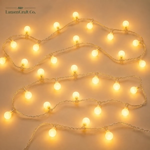 May include: A string of decorative globe lights featuring small, spherical bulbs that emit a warm, golden glow. The bulbs are evenly spaced along a thin, flexible wire. The text LumenCraft Co. appears in the upper left corner of the image.