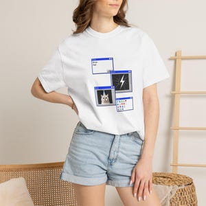 May include: A white short-sleeved t-shirt featuring a graphic print of four computer error windows. One window displays the text Error Fail, another shows a lightning bolt, one contains a cat wearing a party hat, and the last shows various icons.