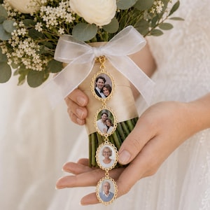 Può includere: Un ciondolo portafoto in metallo dorato con quattro cornici ovali dai bordi smerlati, ognuna contenente una piccola fotografia ritratto. Il ciondolo è fissato a un nastro bianco trasparente legato attorno a un bouquet di fiori bianchi e fogliame verde.