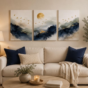 May include: A triptych wall art set featuring abstract watercolour landscapes in shades of navy blue, cream, and gold. The paintings depict rolling hills, a golden sun, and small silhouettes of birds in flight across the three canvas panels.