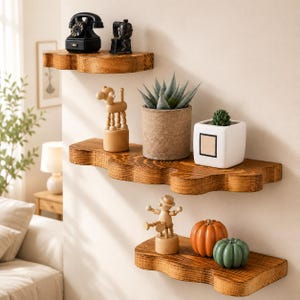 May include: Three wall-mounted wooden shelves with wavy edges. The top shelf holds a black rotary phone and a small black object. The middle shelf holds a wooden animal figure, a succulent in a textured pot, and a white square planter. The bottom shelf holds a wooden jointed figure, an orange pumpkin, and a green pumpkin.
