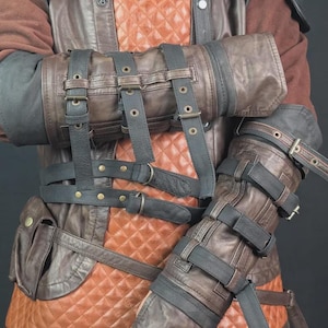 Op de afbeelding: Een bruin en zwart lederen vest met een gewatteerd oranje middenpaneel, meerdere gespriemen en ge&iuml;ntegreerde armbeschermers. Het kledingstuk is voorzien van donkere lederen overlays, metalen gespen en klinknagels, met een kleine zijzak.
