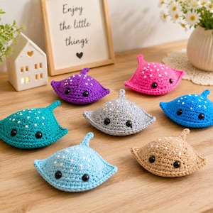 May include: A collection of seven small, handmade crochet stingray plushies in various colors including purple, pink, teal, gray, blue, light blue, and tan. Each stingray features white embroidered spots on the top and two black plastic eyes.